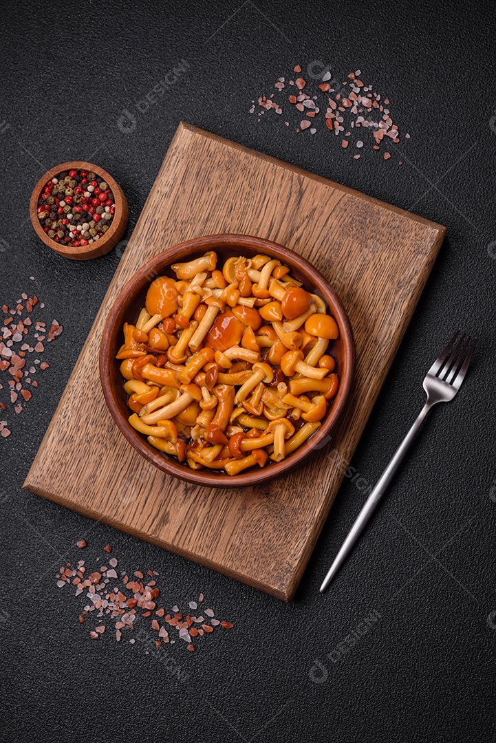 Deliciosos cogumelos em conserva com sal e especiarias em uma placa de cerâmica sobre um fundo escuro e texturizado