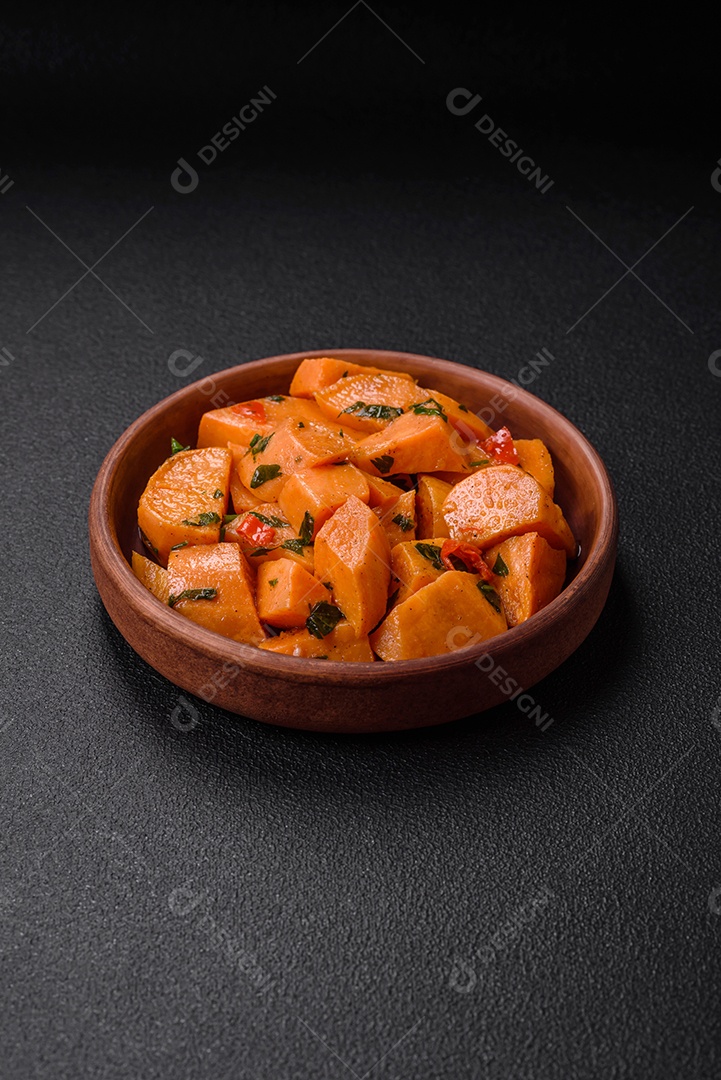 Deliciosa batata-doce cozida com cubos de sal, especiarias e ervas em uma placa cerâmica sobre um fundo escuro de concreto