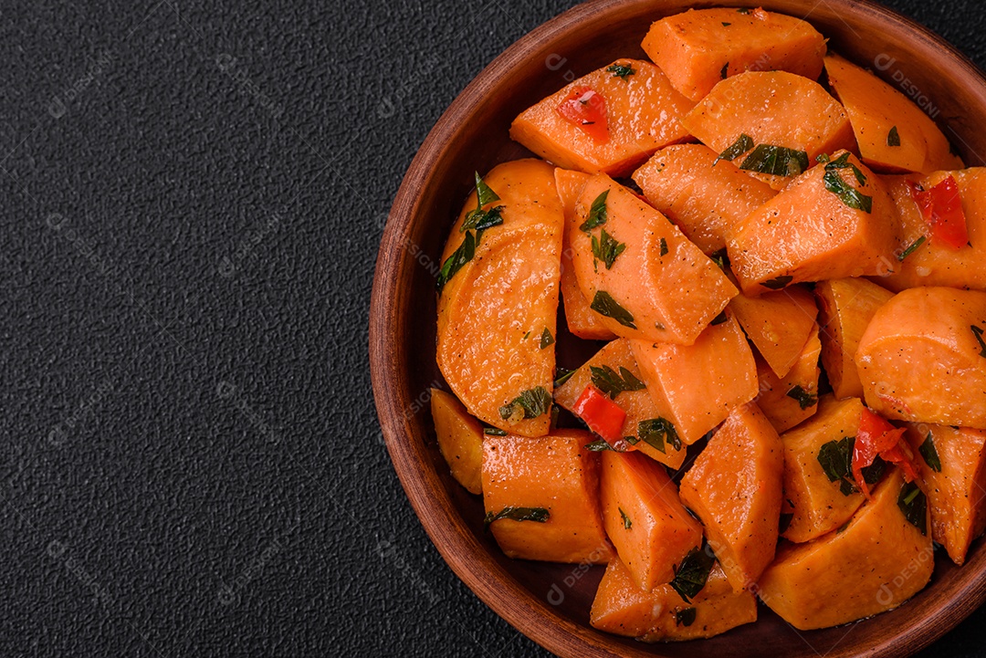 Deliciosa batata-doce cozida com cubos de sal, especiarias e ervas em uma placa cerâmica sobre um fundo escuro de concreto