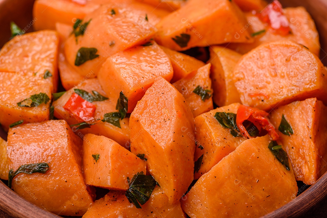 Deliciosa batata-doce cozida com cubos de sal, especiarias e ervas em uma placa cerâmica sobre um fundo escuro de concreto