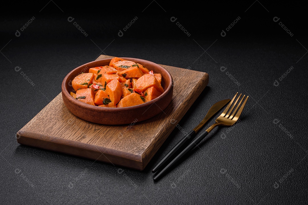 Deliciosa batata-doce cozida com cubos de sal, especiarias e ervas em uma placa cerâmica sobre um fundo escuro de concreto