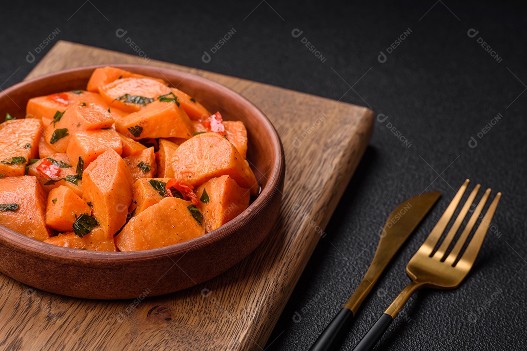 Deliciosa batata-doce cozida com cubos de sal, especiarias e ervas em uma placa cerâmica sobre um fundo escuro de concreto