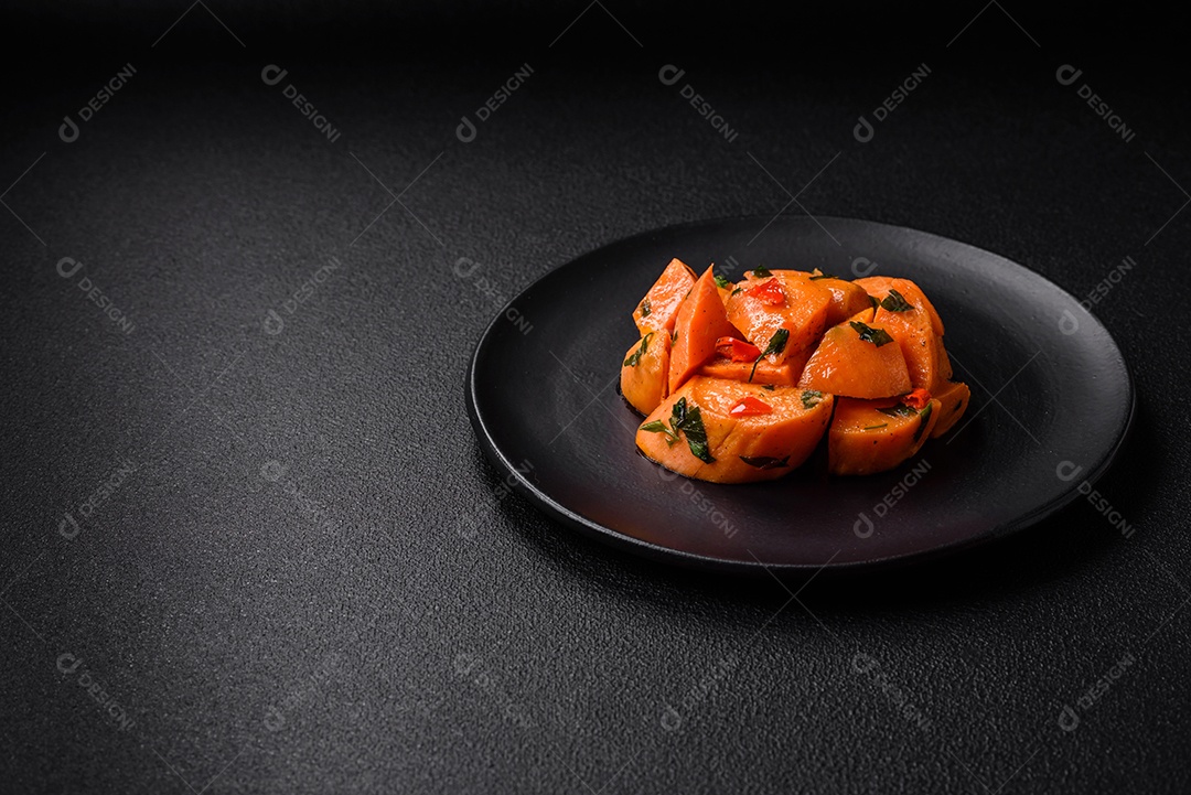 Deliciosa batata-doce cozida com cubos de sal, especiarias e ervas em uma placa cerâmica sobre um fundo escuro de concreto