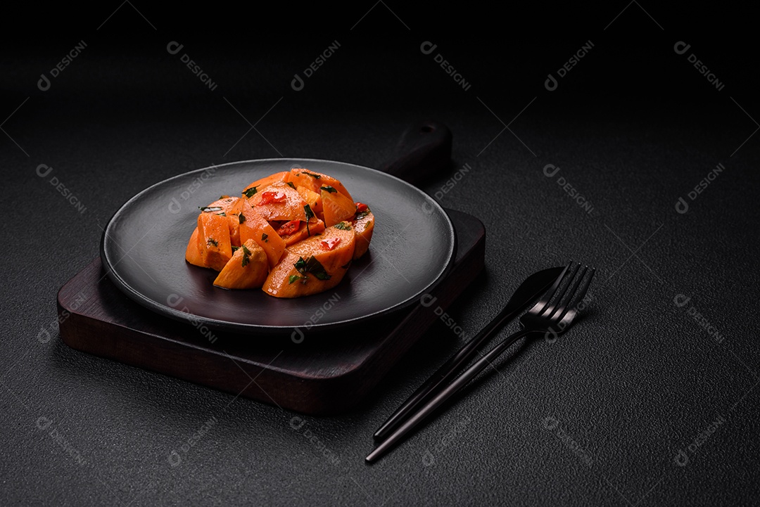 Deliciosa batata-doce cozida com cubos de sal, especiarias e ervas em uma placa cerâmica sobre um fundo escuro de concreto