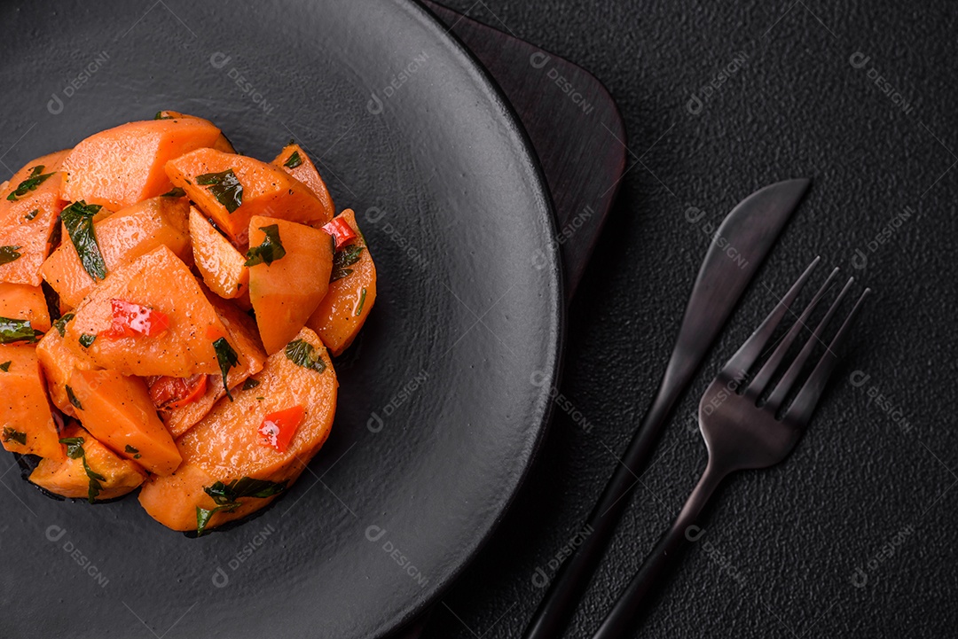 Deliciosa batata-doce cozida com cubos de sal, especiarias e ervas em uma placa cerâmica sobre um fundo escuro de concreto