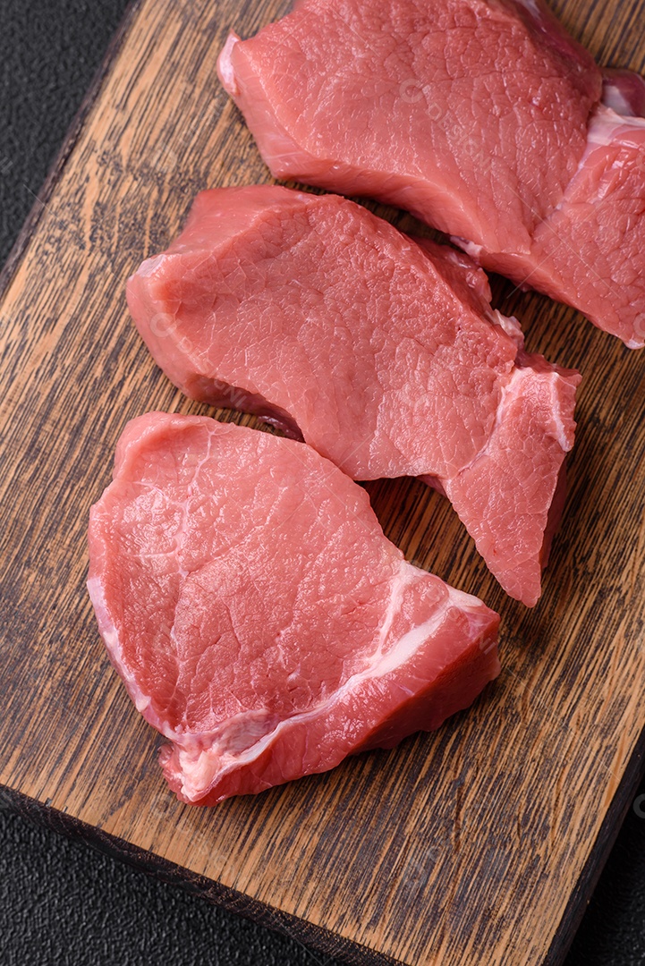 Bife de carne de porco fresca crua com sal, especiarias e ervas numa tábua de madeira