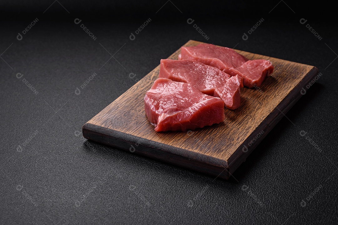 Bife de carne de porco fresca crua com sal, especiarias e ervas numa tábua de madeira
