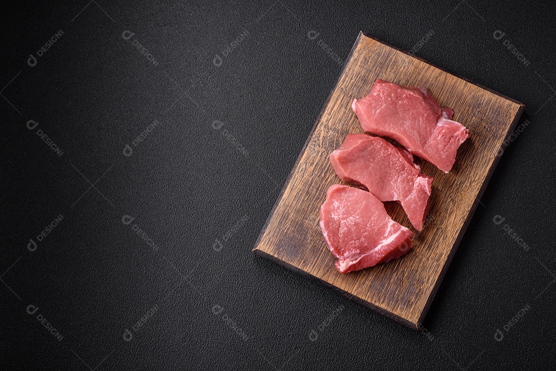 Bife de carne de porco fresca crua com sal, especiarias e ervas numa tábua de madeira