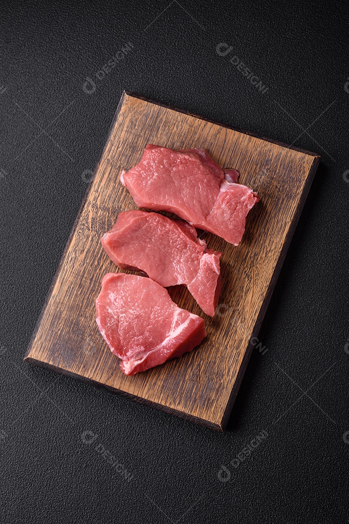 Bife de carne de porco fresca crua com sal, especiarias e ervas numa tábua de madeira