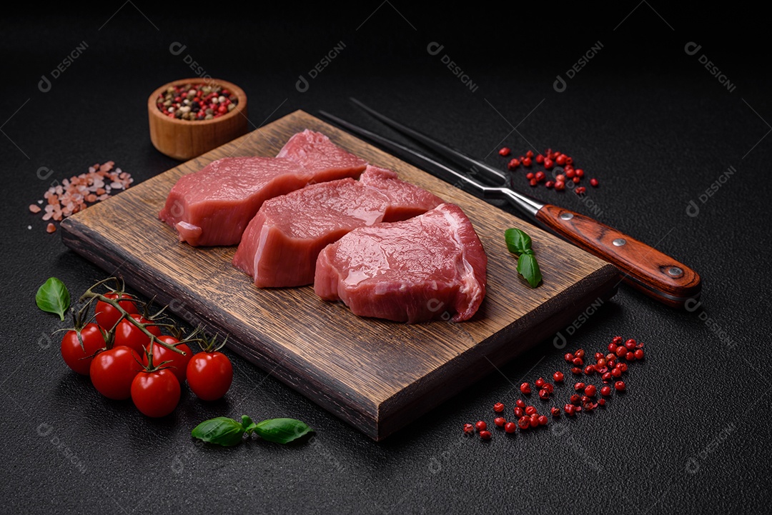 Bife de carne de porco fresca crua com sal, especiarias e ervas numa tábua de madeira