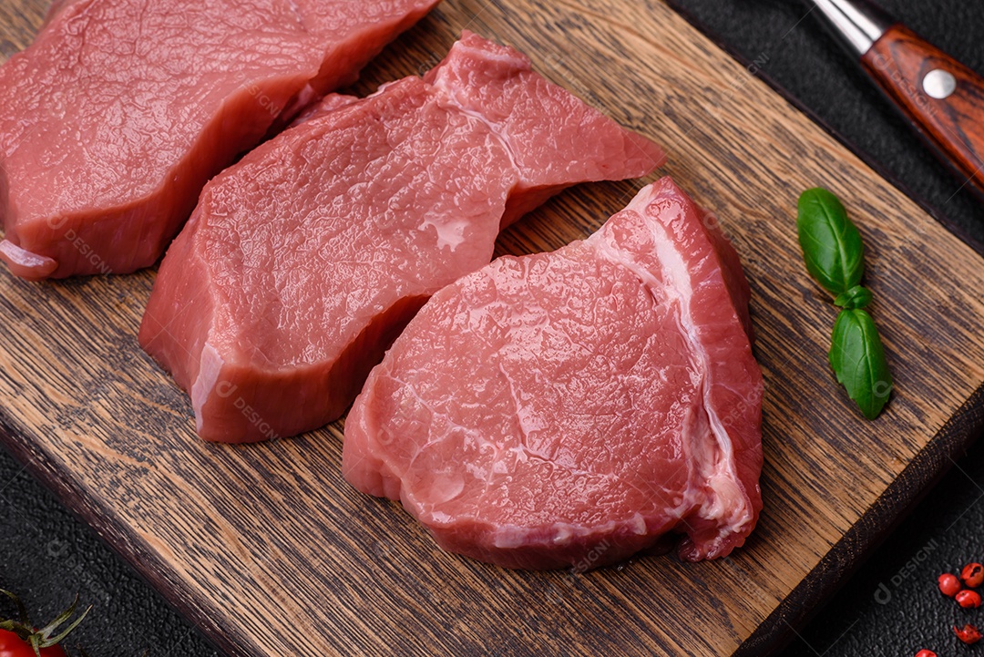 Bife de carne de porco fresca crua com sal, especiarias e ervas numa tábua de madeira