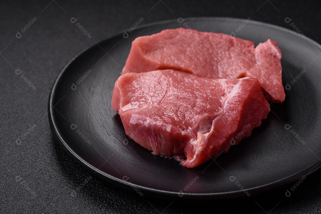 Bife de carne de porco fresca crua com sal, especiarias e ervas numa tábua de madeira