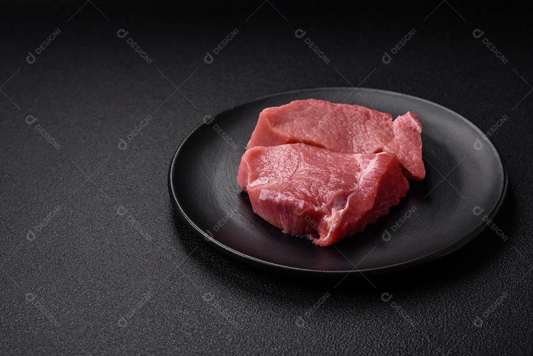 Carne de peru crua em forma de fatias com sal, especiarias e ervas sobre um fundo escuro de concreto