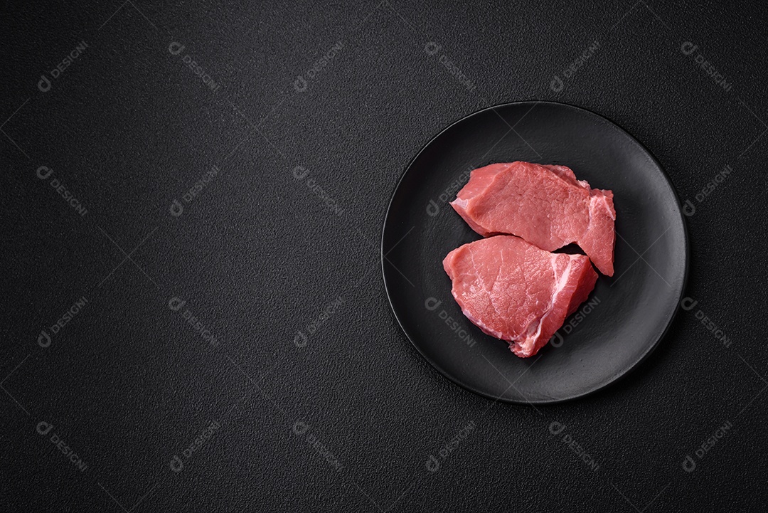 Bife de carne de porco fresca crua com sal, especiarias e ervas numa tábua de madeira