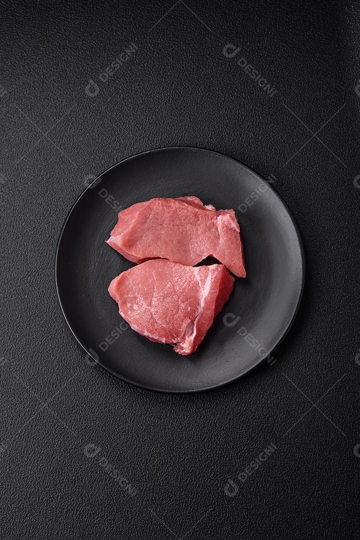 Bife de carne de porco fresca crua com sal, especiarias e ervas numa tábua de madeira