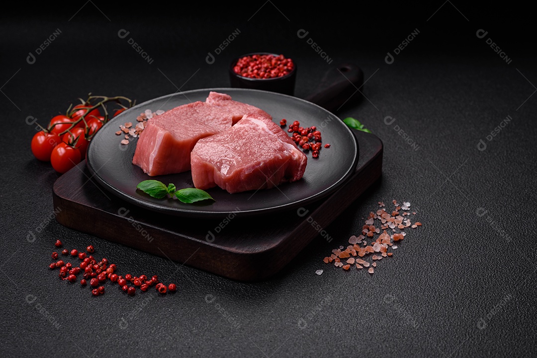 Bife de carne de porco fresca crua com sal, especiarias e ervas numa tábua de madeira