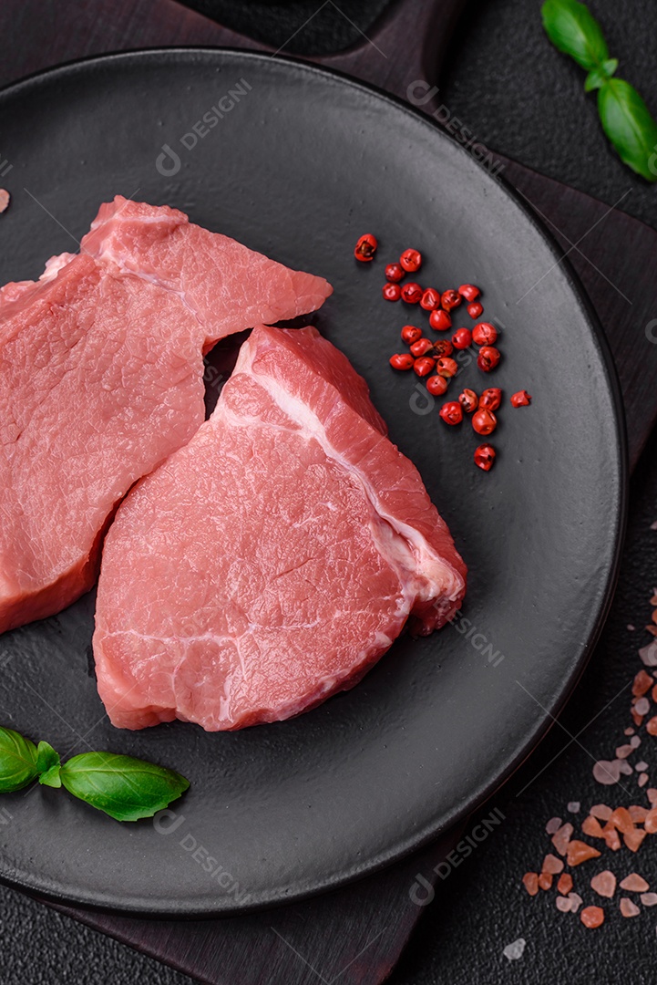 Bife de carne de porco fresca crua com sal, especiarias e ervas numa tábua de madeira