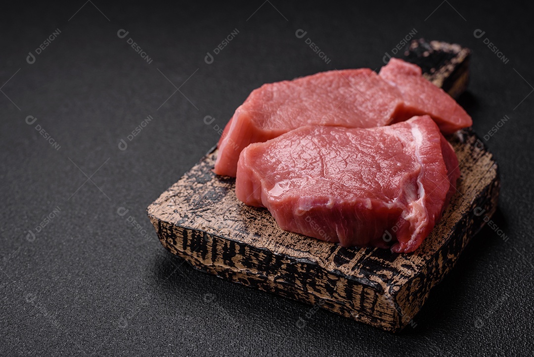 Bife de filé mignon cru com sal, especiarias e ervas em um fundo escuro de concreto