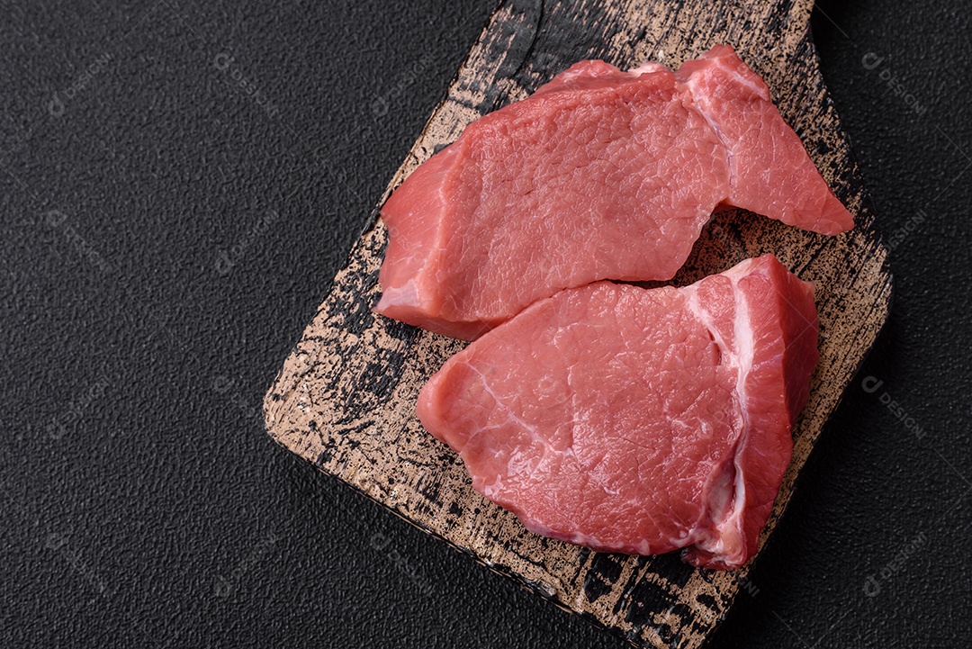 Bife de carne de porco fresca crua com sal, especiarias e ervas numa tábua de madeira