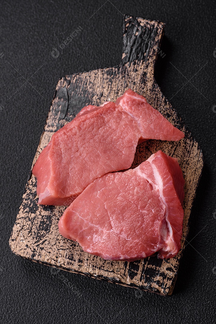 Bife de filé mignon cru com sal, especiarias e ervas em um fundo escuro de concreto