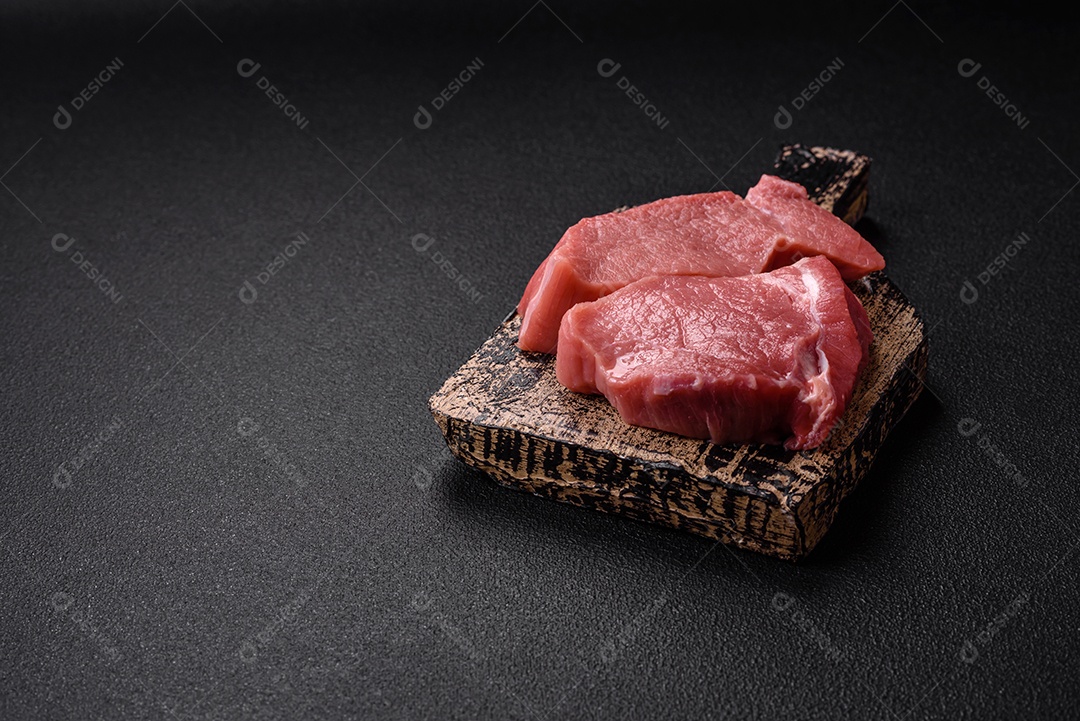 Bife de filé mignon cru com sal, especiarias e ervas em um fundo escuro de concreto
