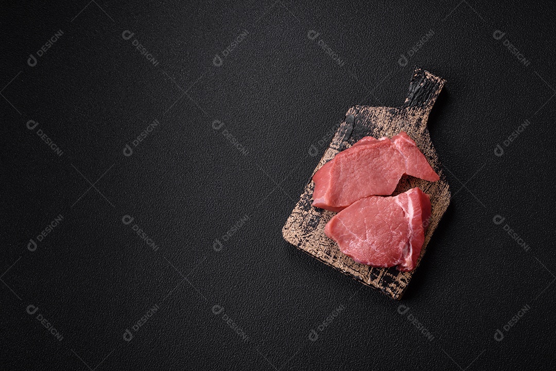 Bife de filé mignon cru com sal, especiarias e ervas em um fundo escuro de concreto
