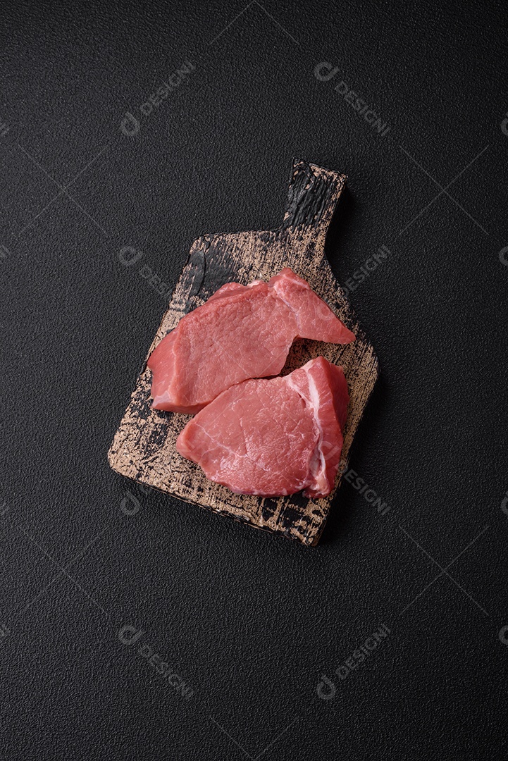 Bife de filé mignon cru com sal, especiarias e ervas em um fundo escuro de concreto