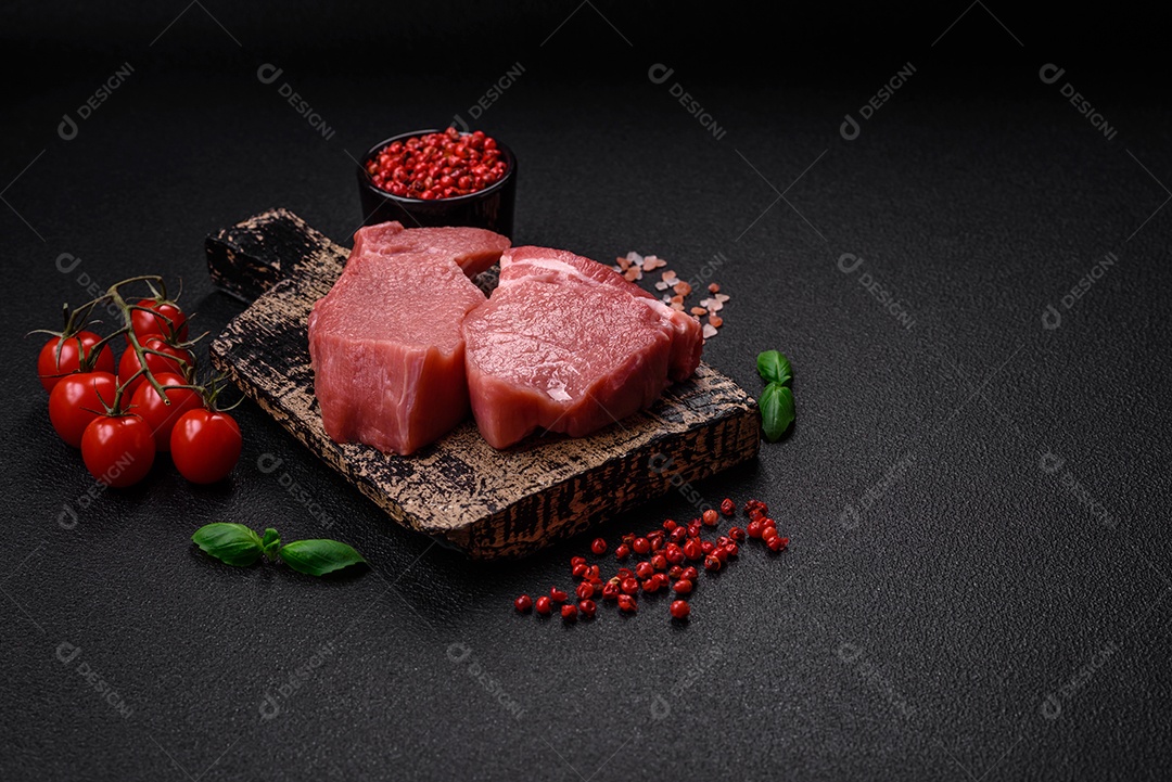 Bife de filé mignon cru com sal, especiarias e ervas em um fundo escuro de concreto