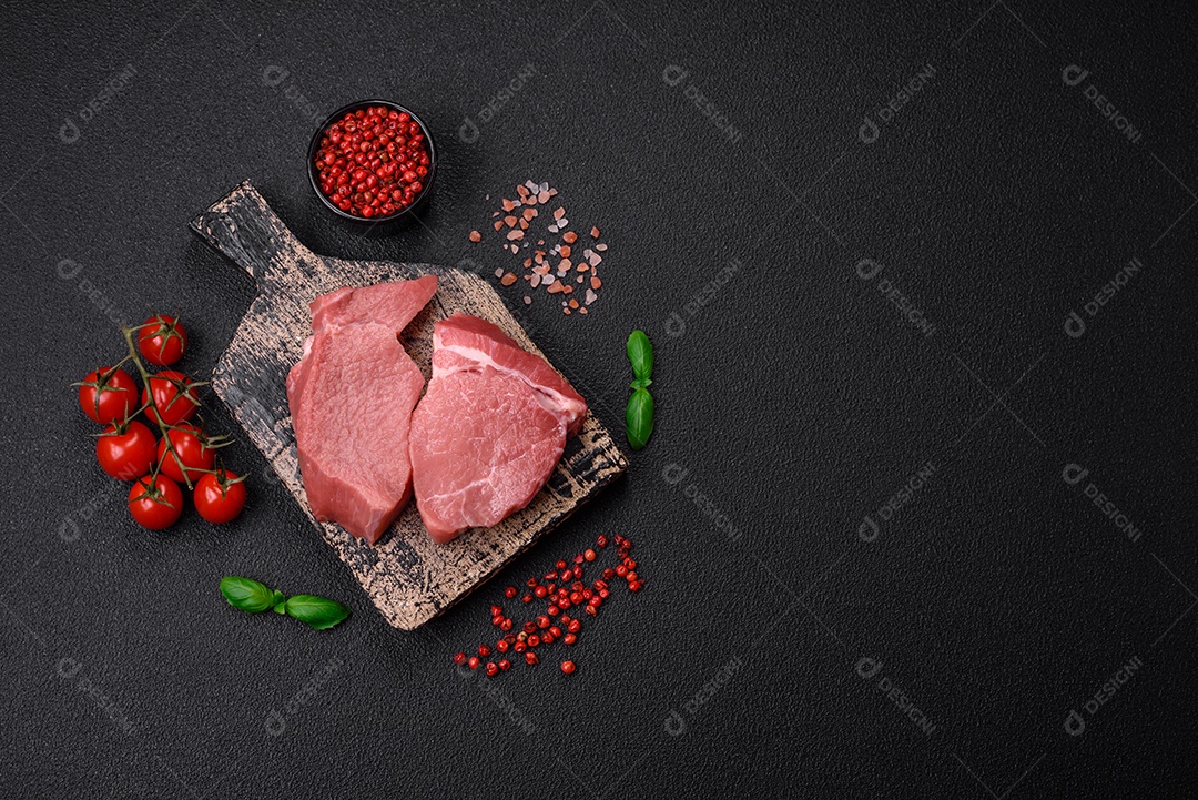 Bife de filé mignon cru com sal, especiarias e ervas em um fundo escuro de concreto