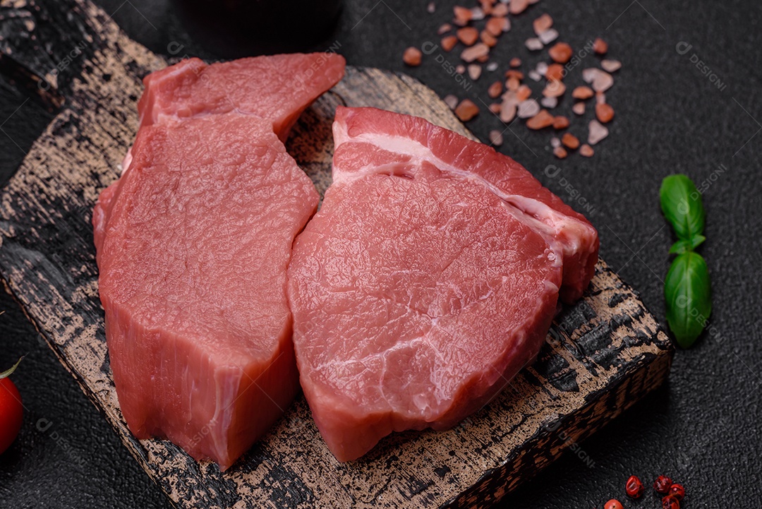 Bife de filé mignon cru com sal, especiarias e ervas em um fundo escuro de concreto