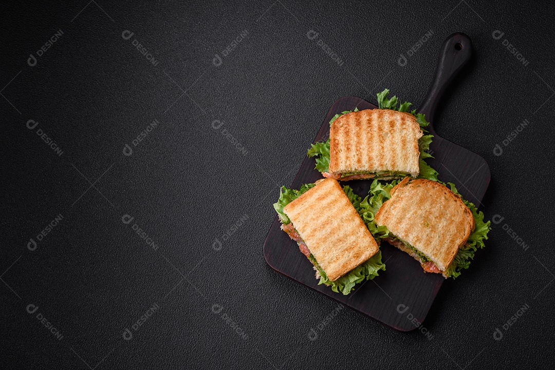 Delicioso sanduíche crocante com torradas, salmão, abacate, tomate, sal, especiarias e ervas sobre um fundo escuro de concreto