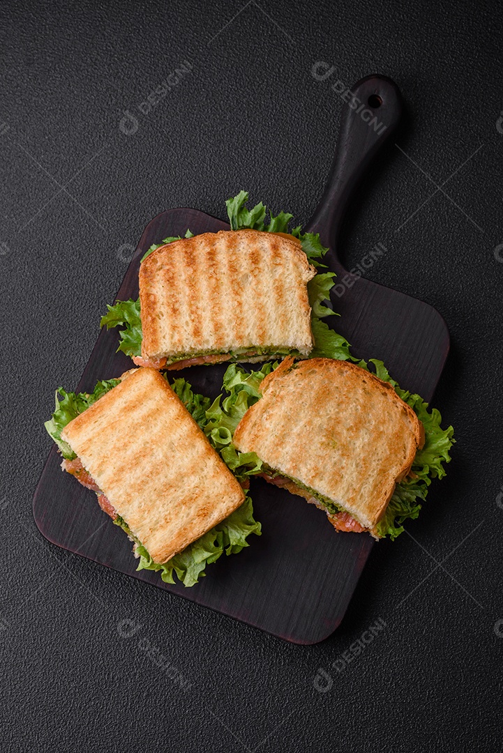 Delicioso sanduíche crocante com torradas, salmão, abacate, tomate, sal, especiarias e ervas sobre um fundo escuro de concreto
