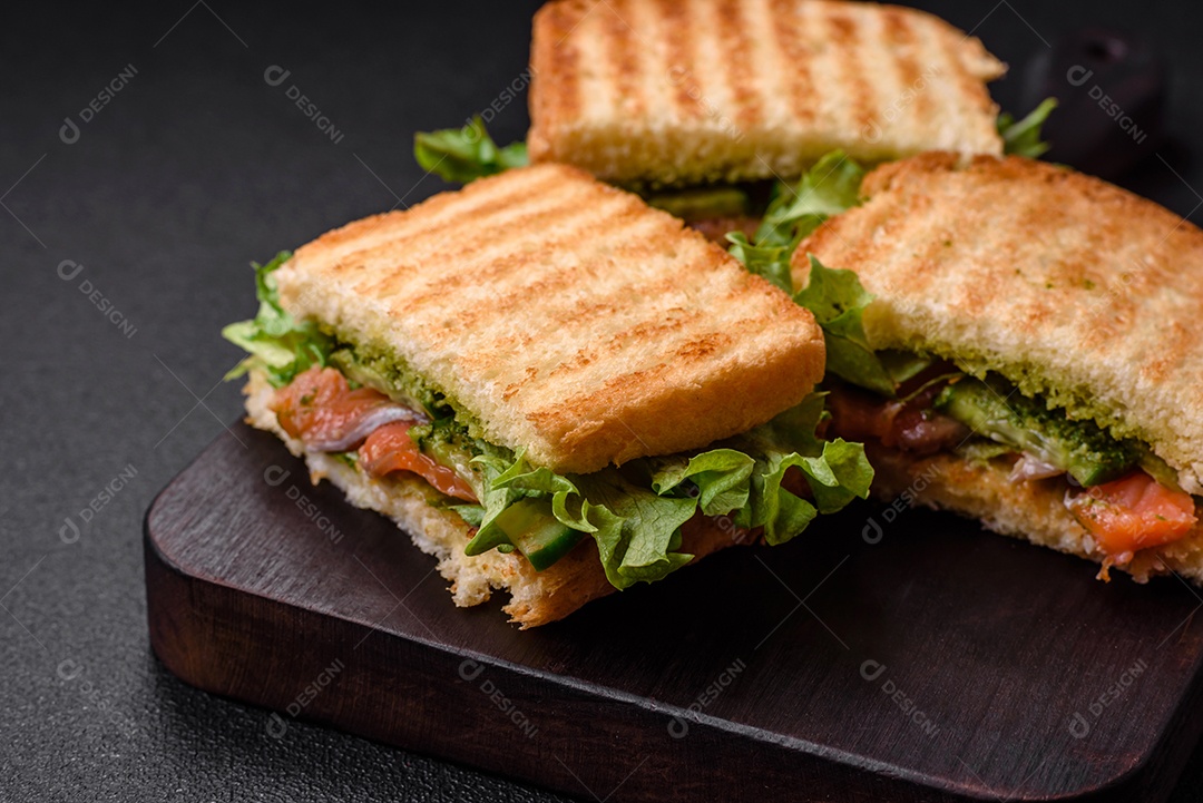 Delicioso sanduíche crocante com torradas, salmão, abacate, tomate, sal, especiarias e ervas sobre um fundo escuro de concreto