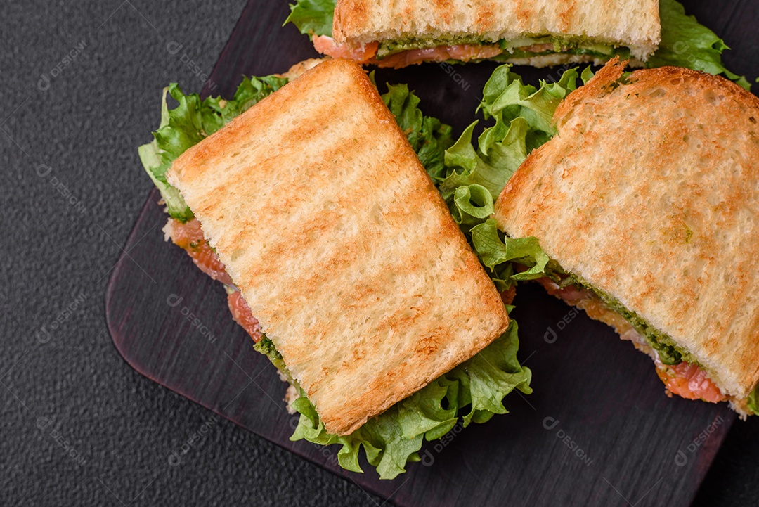Delicioso sanduíche crocante com torradas, salmão, abacate, tomate, sal, especiarias e ervas sobre um fundo escuro de concreto