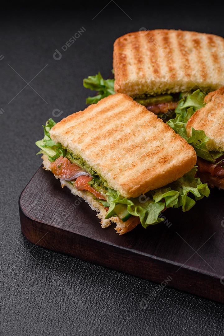 Delicioso sanduíche crocante com torradas, salmão, abacate, tomate, sal, especiarias e ervas sobre um fundo escuro de concreto