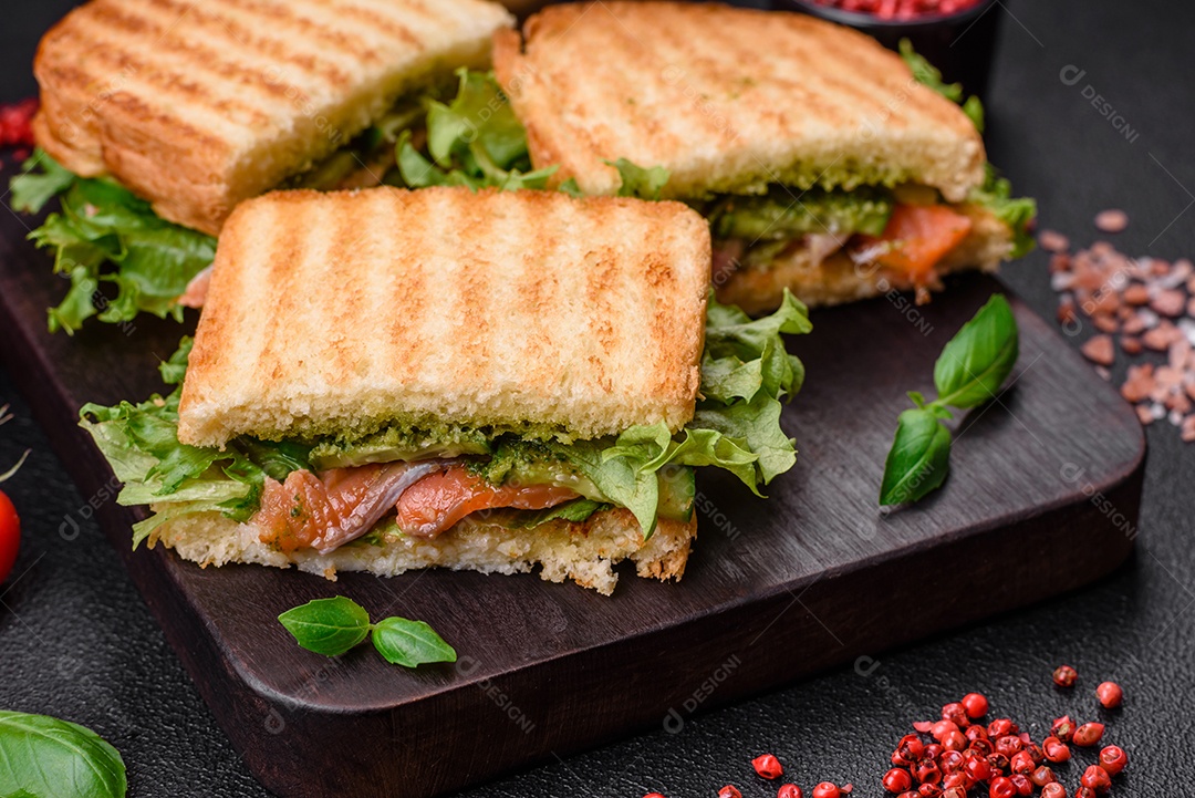 Delicioso sanduíche crocante com torradas, salmão, abacate, tomate, sal, especiarias e ervas sobre um fundo escuro de concreto