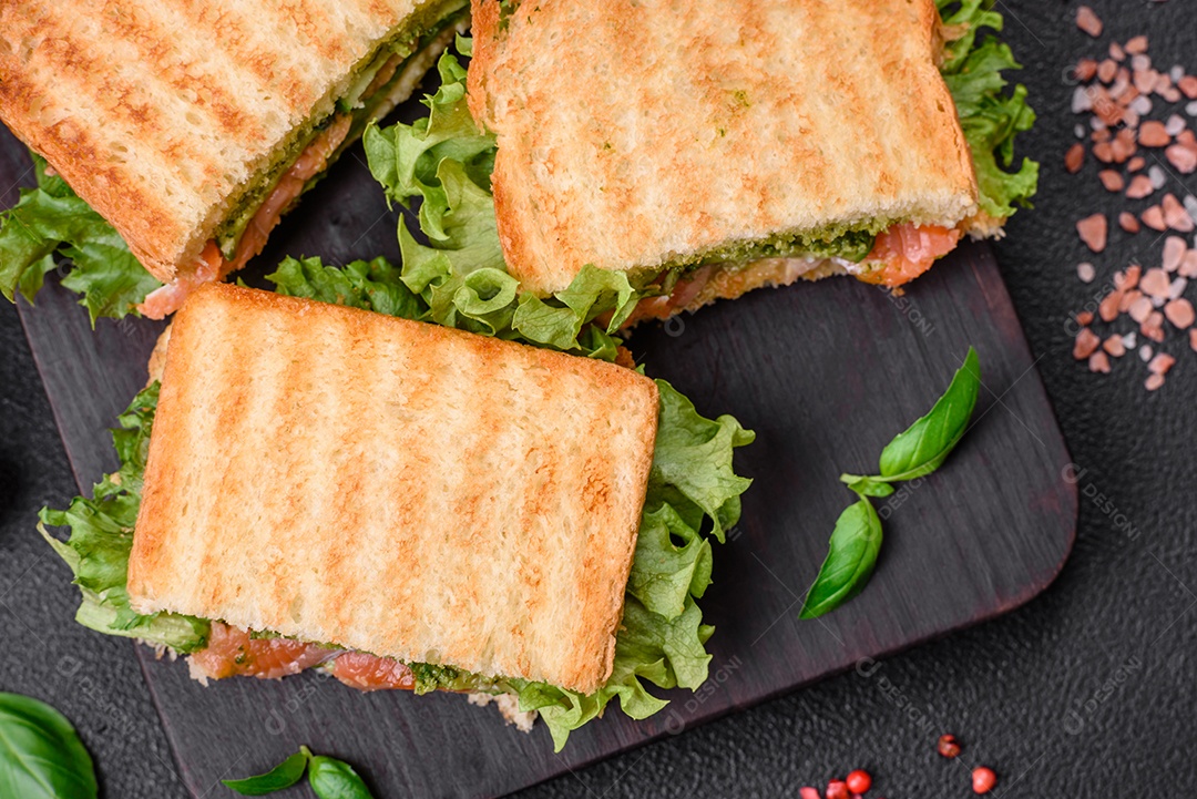 Delicioso sanduíche crocante com torradas, salmão, abacate, tomate, sal, especiarias e ervas sobre um fundo escuro de concreto