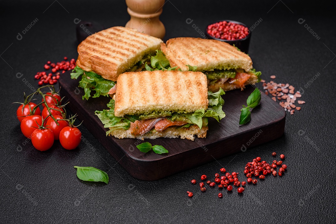 Delicioso sanduíche crocante com torradas, salmão, abacate, tomate, sal, especiarias e ervas sobre um fundo escuro de concreto