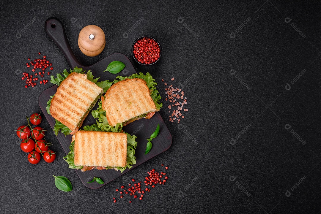 Delicioso sanduíche crocante com torradas, salmão, abacate, tomate, sal, especiarias e ervas sobre um fundo escuro de concreto