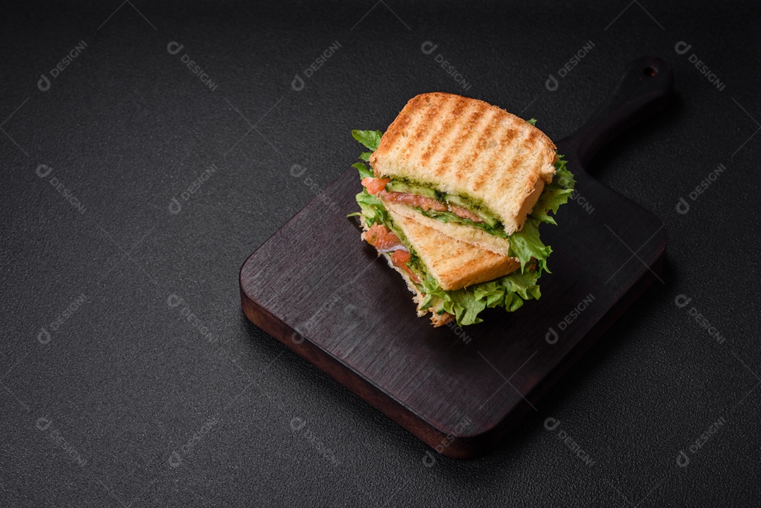 Delicioso sanduíche crocante com torradas, salmão, abacate, tomate, sal, especiarias e ervas sobre um fundo escuro de concreto