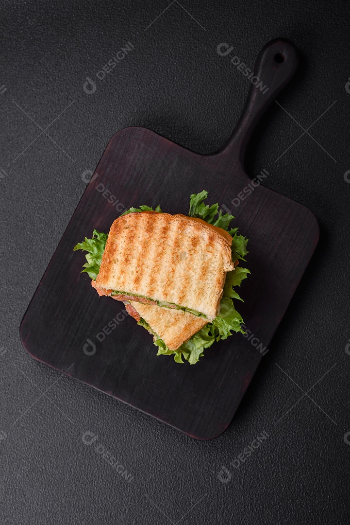 Delicioso sanduíche crocante com torradas, salmão, abacate, tomate, sal, especiarias e ervas sobre um fundo escuro de concreto