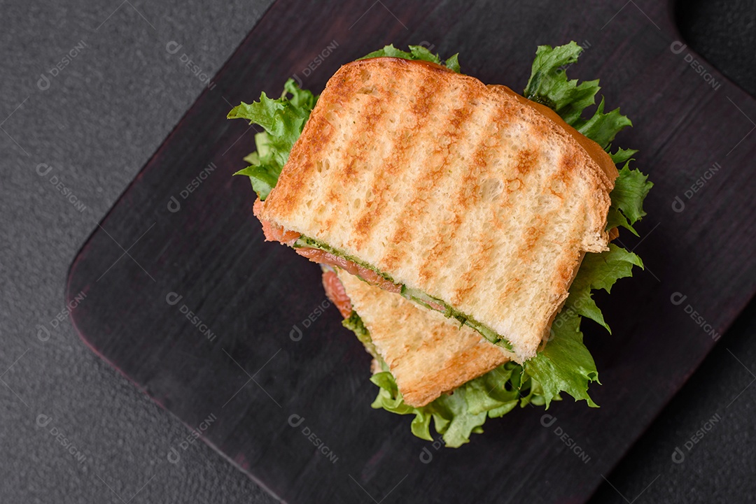 Delicioso sanduíche crocante com torradas, salmão, abacate, tomate, sal, especiarias e ervas sobre um fundo escuro de concreto