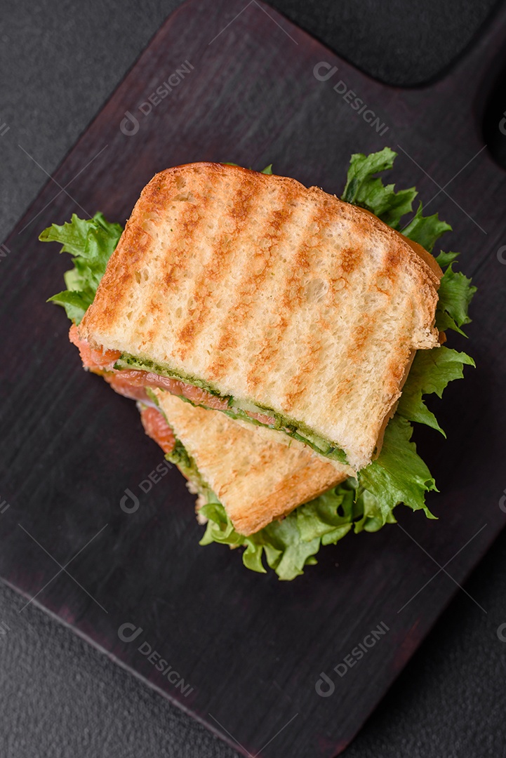 Delicioso sanduíche crocante com torradas, salmão, abacate, tomate, sal, especiarias e ervas sobre um fundo escuro de concreto