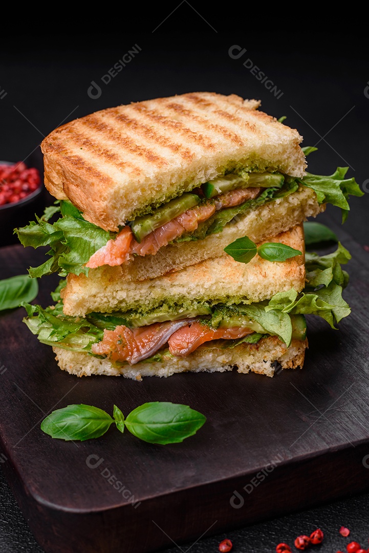 Delicioso sanduíche crocante com torradas, salmão, abacate, tomate, sal, especiarias e ervas sobre um fundo escuro de concreto
