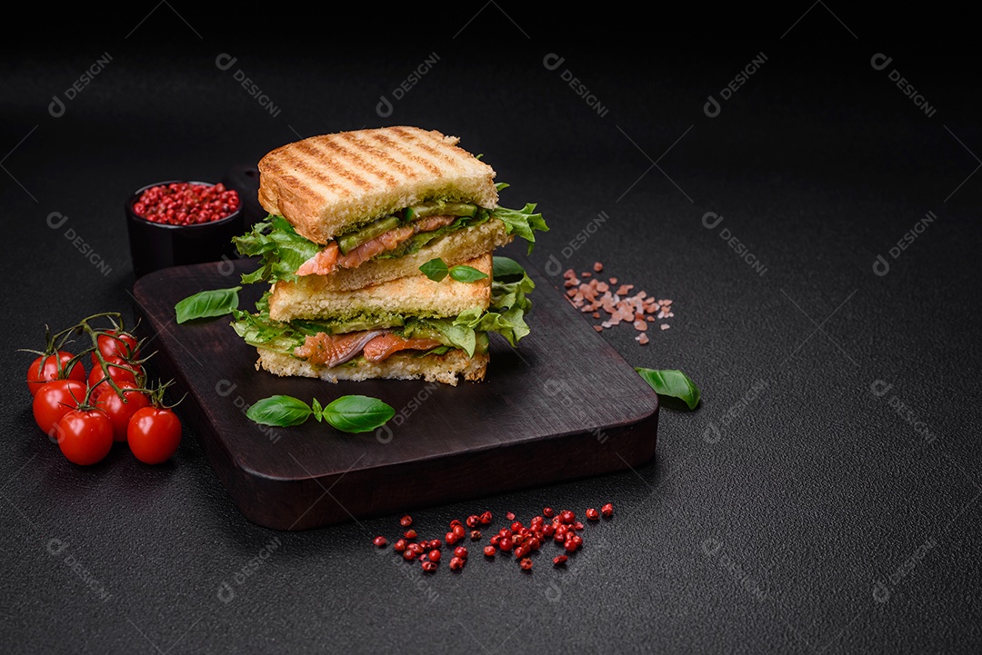 Delicioso sanduíche crocante com torradas, salmão, abacate, tomate, sal, especiarias e ervas sobre um fundo escuro de concreto