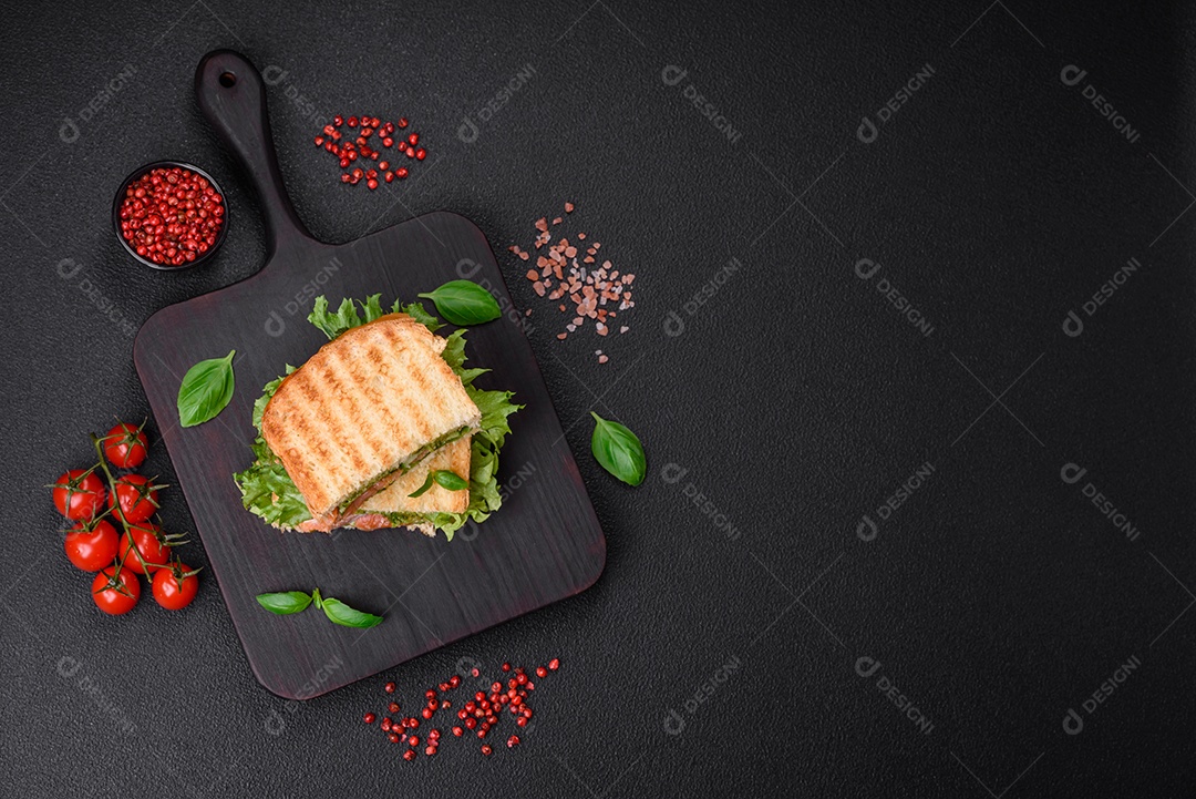 Delicioso sanduíche crocante com torradas, salmão, abacate, tomate, sal, especiarias e ervas sobre um fundo escuro de concreto