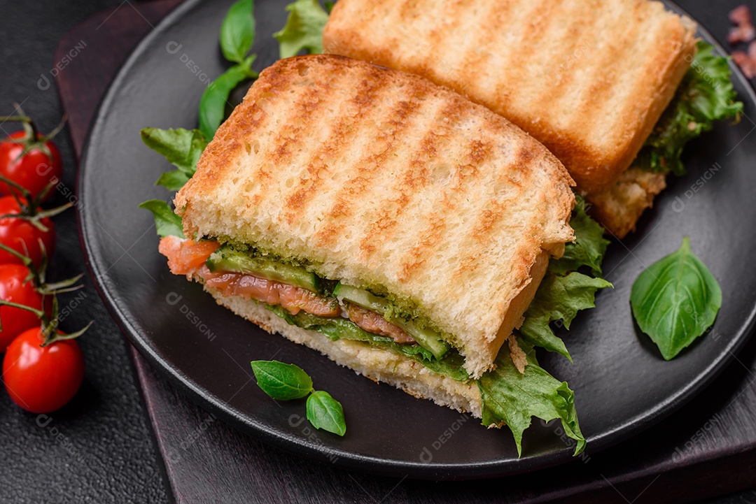 Delicioso sanduíche crocante com torradas, salmão, abacate, tomate, sal, especiarias e ervas sobre um fundo escuro de concreto