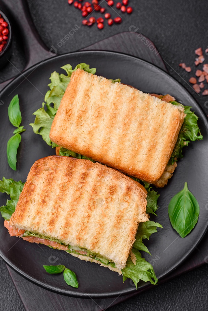 Delicioso sanduíche crocante com torradas, salmão, abacate, tomate, sal, especiarias e ervas sobre um fundo escuro de concreto