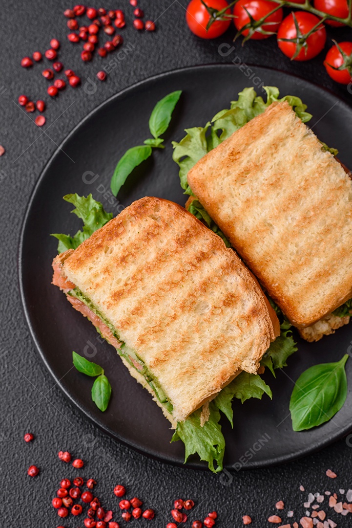 Delicioso sanduíche crocante com torradas, salmão, abacate, tomate, sal, especiarias e ervas sobre um fundo escuro de concreto