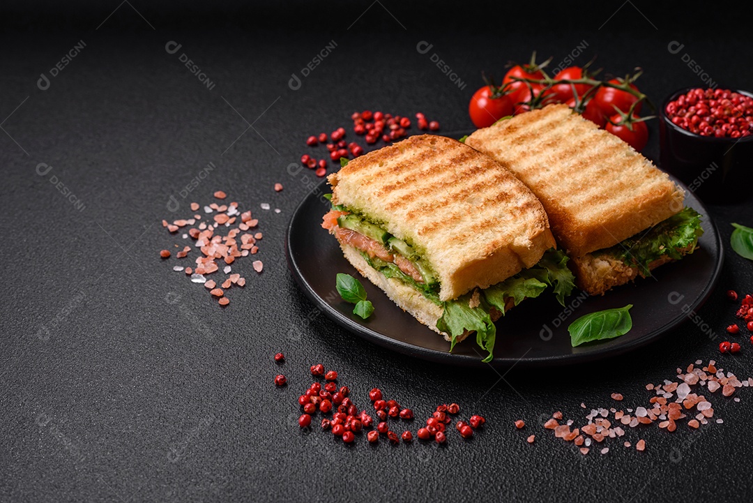 Delicioso sanduíche crocante com torradas, salmão, abacate, tomate, sal, especiarias e ervas sobre um fundo escuro de concreto